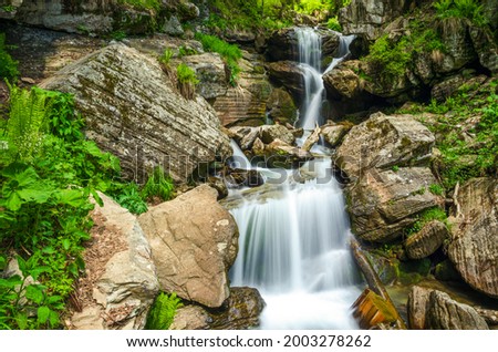 The waterfall cascade flows along the stone threshold, in a subtropical forest, long exposure. Mendelikha Waterfall, Rosa Khutor, Sochi-Russia
