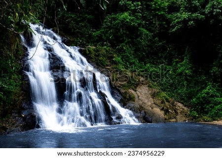 A waterfall cascades down a rocky cliff into a clear pool of water. The waterfall is surrounded by lush green trees, and the sound of the water is calming.
