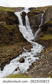 Rjúkandafoss waterfall cascades down rugged cliffs into a rushing stream, Iceland.