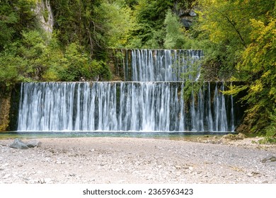 Waterfall cascades on the Pisnica river, Kranjska Gora, Slovenia, Triglav National Park. Autumn landscape with falling water surrounded by wooded cliffs, outdoor travel background