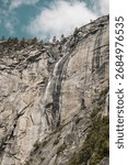 Waterfall cascading down granite cliffs in Yosemite National Park, California, with scattered clouds above the Sierra Nevada landscape.