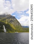 Waterfall cascading off mountain side in Fiordland National Park New Zealand on partially cloudy day