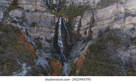 Waterfall comes down side of mountain in fall with rocks and trees