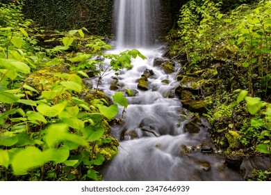 Waterfall and creek or brook in Iserlohn Sauerland Germany after heavy rain. Long time exposure of falling and flowing water in motion with wet rocks, stones and bright green springtime vegetation.