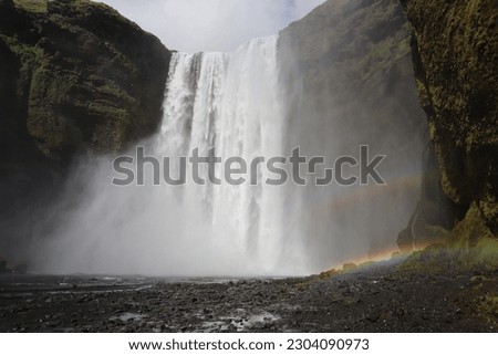 A waterfall falls from a large cliff with a rainbow beside it in Iceland