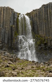 Waterfall flowing between dramatic basalt rock columns in natural volcanic landscape.