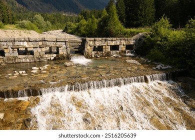 Waterfall flowing under a stone bridge in a serene alpine landscape, surrounded by lush forest and mountains, showcasing natural tranquility - Powered by Shutterstock