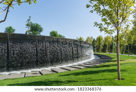 Waterfall flows in streams into granite bed of artificial river. Fountain in form of huge bowl. Public landscape city park Krasnodar or 'Galitsky park' for relaxation and walking in sunny autumn 2020