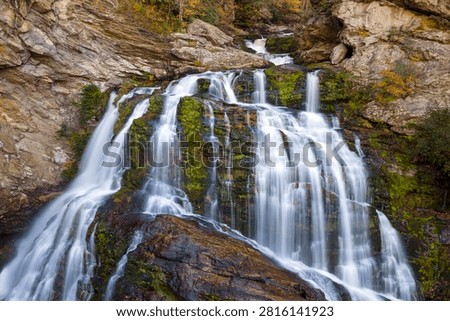 Waterfall flows through vibrant fall forest in remote gorge. Cullasaja Falls in November, nestled in the wooded mountains of North Carolina, USA.