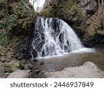 waterfall into a pool of water surrounded by cluffs and vegetation. large rocks in the foreground 