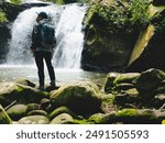 Waterfall in the rainforest on the walkway and adventurer hiker with backpack standing in front of tropical waterfall in Phu Soi Dao National Park, Thailand.