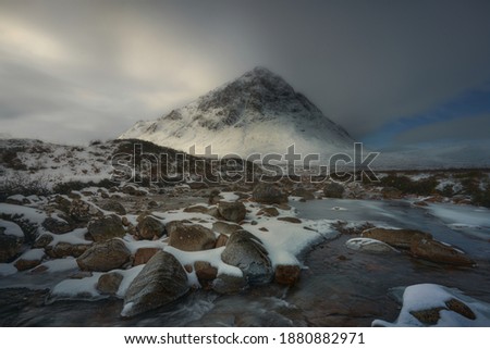 Waterfall to River Etive, Glencoe, Scotland, Uk. River with lots of water, picture in the forest with Stob Dearg mountain in the background. Snowy atmosphere in winter, after a big storm
