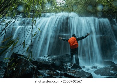 Waterfall with tourist, Hiker with backpack enjoying the beauty of tropical waterfall, Kerala travel and tourism concept image, Happy man raising arms up looking at forest waterfall - Powered by Shutterstock