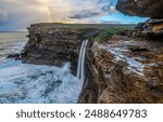 The waterfall from the valley breaks into the ocean. Waterfall in ocean. Mountain valley waterfall. Beautiful waterfall