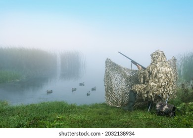 Waterfowl Hunter With Gun In Duck Hunting Shelter At Sunrise. 