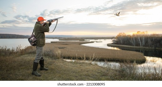  waterfowl hunter shooting into sky during duck hunting at sunrise. hunting banner