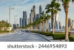 Waterfront promenade on the Palm Jumeirah with palms at road and traffic timelapse before sunset. Dubai, United Arab Emirates. Dubai marina towers on background