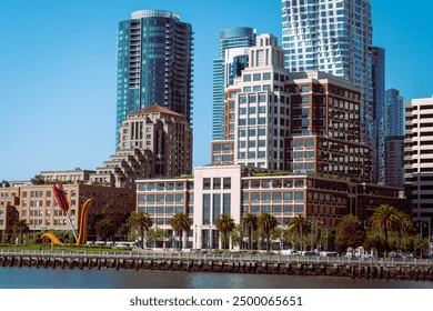 a waterfront view of a modern cityscape with high-rise buildings and a prominent sculpture in the foreground. Palm trees line the waterfront, adding a touch of greenery to the urban scene. - Powered by Shutterstock