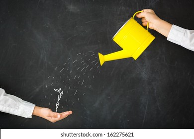 Watering can in hand against blackboard - Powered by Shutterstock