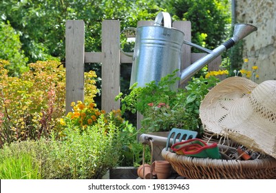 Watering Can Hanging On A Fence And Gardening Basket With Straw Hat