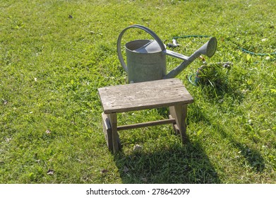 Watering Can And Stool In A Garden, Poland.