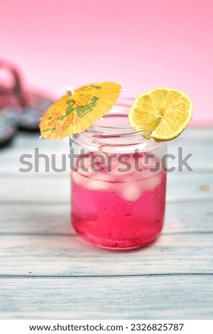 Watermelon drink with vodka with an umbrella and a slice of lemon on a wooden table and a pink background.