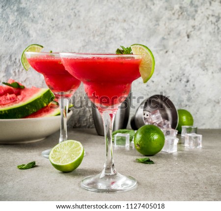 Watermelon margarita cocktail with lime and sliced watermelon, light concrete background copy space