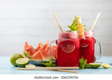 Watermelon mojito fresh red drink. With watermelon, lemon, lime, mint leaves and ice. The drink is on a white table with a cut watermelon in the background. - Powered by Shutterstock