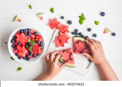 Watermelon salad. Slices of watermelon in the shape of a star. Children's hands cooking fruit salad on white table. Top view, flat lay