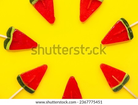 Watermelon slice lollipops arranged in a circle on bright yellow background, sweet candy treats for summer fun