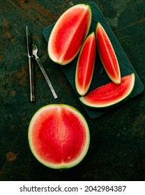 Watermelon slices on a dark moody background. Red fresh organic watermelon on a rusty modern background with cutlery.