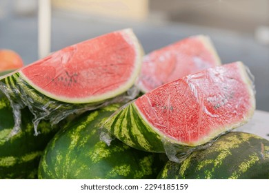 Watermelons in the market. Fresh watermelons are stacked on the counter, cut into pieces and wrapped in plastic wrap to keep fresh.