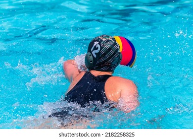 Waterpolo game swimmer girl female player unrecognizable behind rear photo with ball in hand play action closeup .