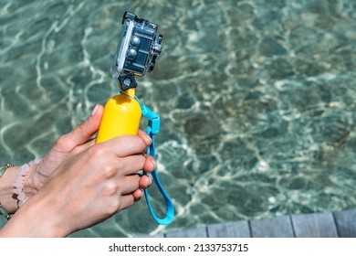 Waterproof action camera with a yellow float in the hands of a girl. Against the background of the water in the pool