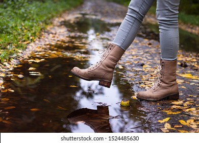 Waterproof leather boots over puddle with reflection. Hiking boot at autumn season. Woman walking on wet footpath after rain