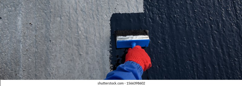 Waterproofing coating. Worker applies bitumen mastic on the foundation. Roofer cover the rooftop polymer modified bitumen waterproofing primer, with a paint brush.