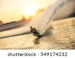 Waterskier moving fast in splashes of water at sunset. Man wakeboarding on a lake