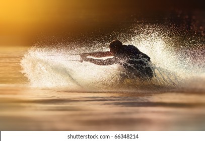 Waterskier silhouette moving fast in splashes of water at sunset