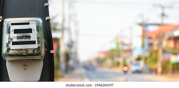 Watthour Metre Of Electricity Hanging On Pole Beside The Rural Road, Blurred Background.