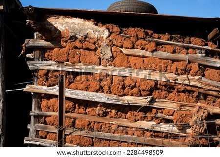 A wattle and daub wall of a rural shack constructed of red clay and wood.