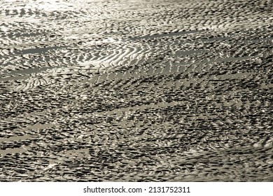 Wave action as the tide recedes has left a pattern of dune-like ripples on a sandy beach. They look like a desert in miniature, created by similar erosive forces in water as with the winds
