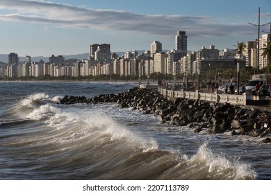Wave approaching the shore during high tide. Beach wall and waterfront buildings in the city of Santos, Brazil.