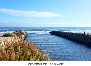 Wave Breaker And Stone Pier At Sea. The River Flows Into The Sea. View Of The Mediterranean Sea With The River At Rocky Shore. Coastline Of The Island. Wave Breakers Along The Shoreline At Ocean. 