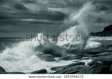 Wave breaking on rocky shore under cloudy sky