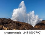 Wave crashing against rocks at Point Lobos Nature Preserve, Monterey, California. Spray thrown high into the air. Pacific ocean and clear blue sky in the background.
