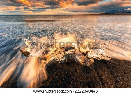 Wave crashing iceberg melting on black sand beach in the sunset at Diamond Beach, Iceland