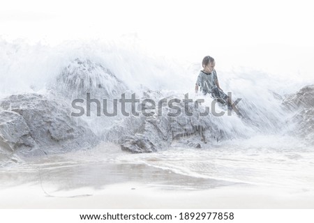 Wave is lapping little boy who sit on the rock.