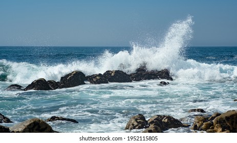 Wave splashing against rocks in the ocean, sending spray into the air. Bright sunny day in summer.