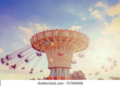 Wave Swinger ride against blue sky, vintage filter effects - a swinging carousel fair ride in amusement park at dusk