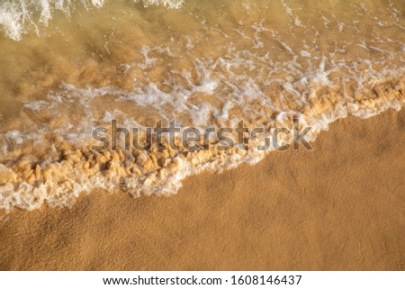 Waves breaking on an empty sand beach and spalsh producing white foam - travel holiday vacation summer season sun splashing water wavy golden yellow sand sandy background blue azure yellow aquamarine